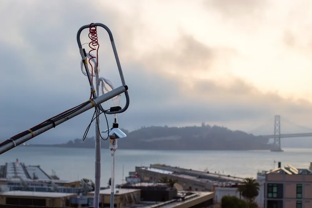 Weather-balloon launch hardware above a waterfront, with a bridge in the distance.