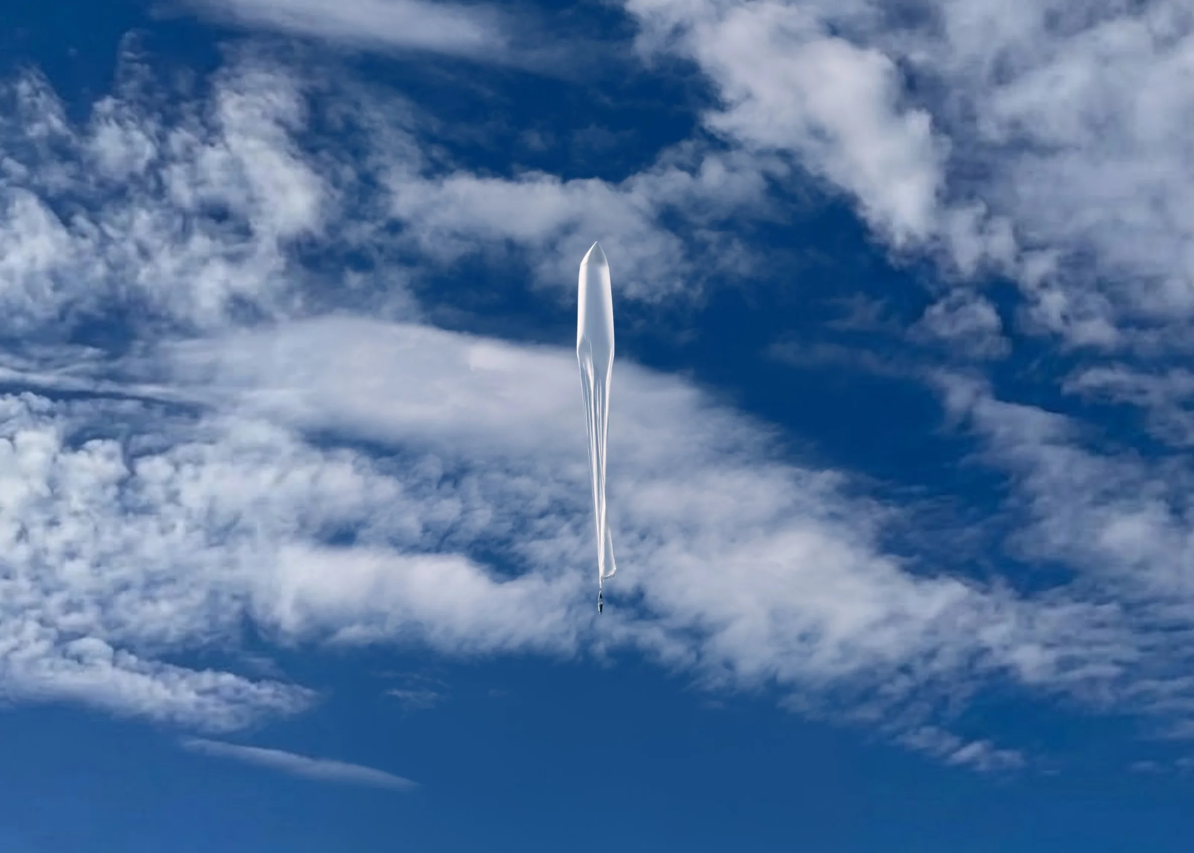 A WindBorne atmospheric balloon flying in a blue sky filled with sweeping clouds