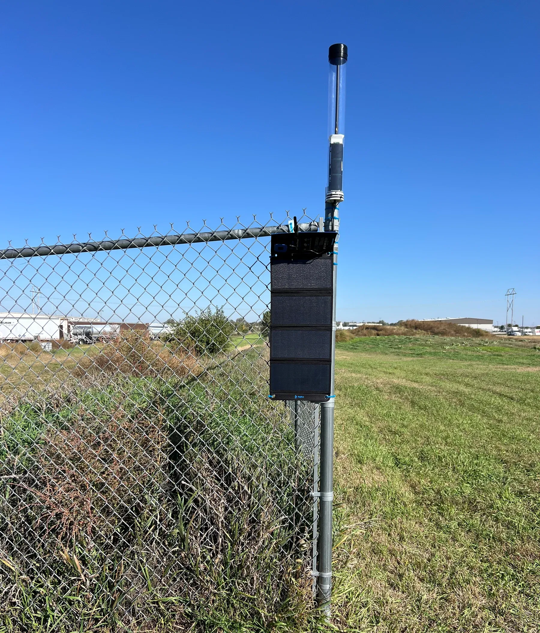 A Comms Nerve antenna and solar panel mounted on a fence beside an open field