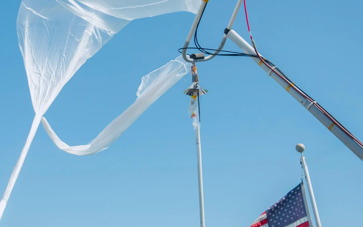WindBorne balloon being inflated on a launch rig. Clear blue sky and American flag flying in the wind.