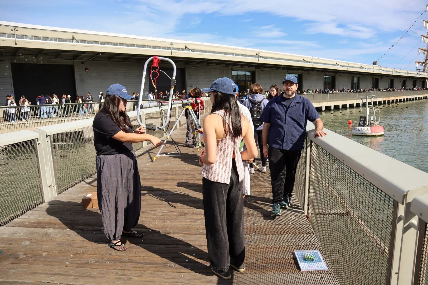 WindBorne team members wearing “Let’s talk about the weather” hats beside a balloon launch rig outside the Exploratorium in San Francisco