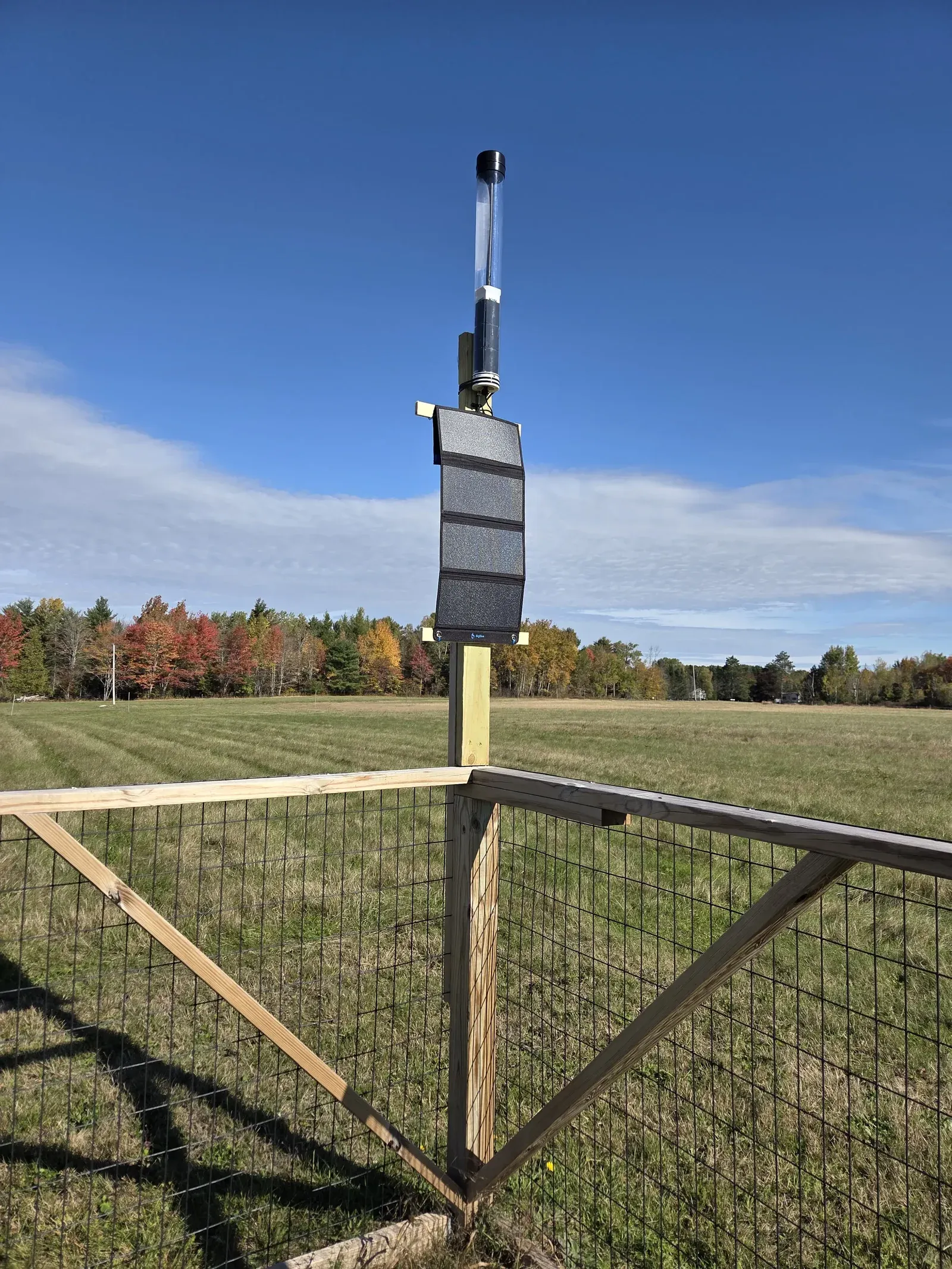A solar-powered WindBorne Comms Nerve mounted on a wooden fence beside an open field