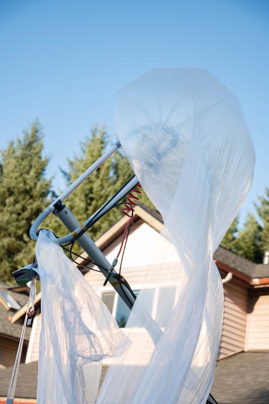 The clear balloon envelope, partly inflated, on the launch rig outside a house.