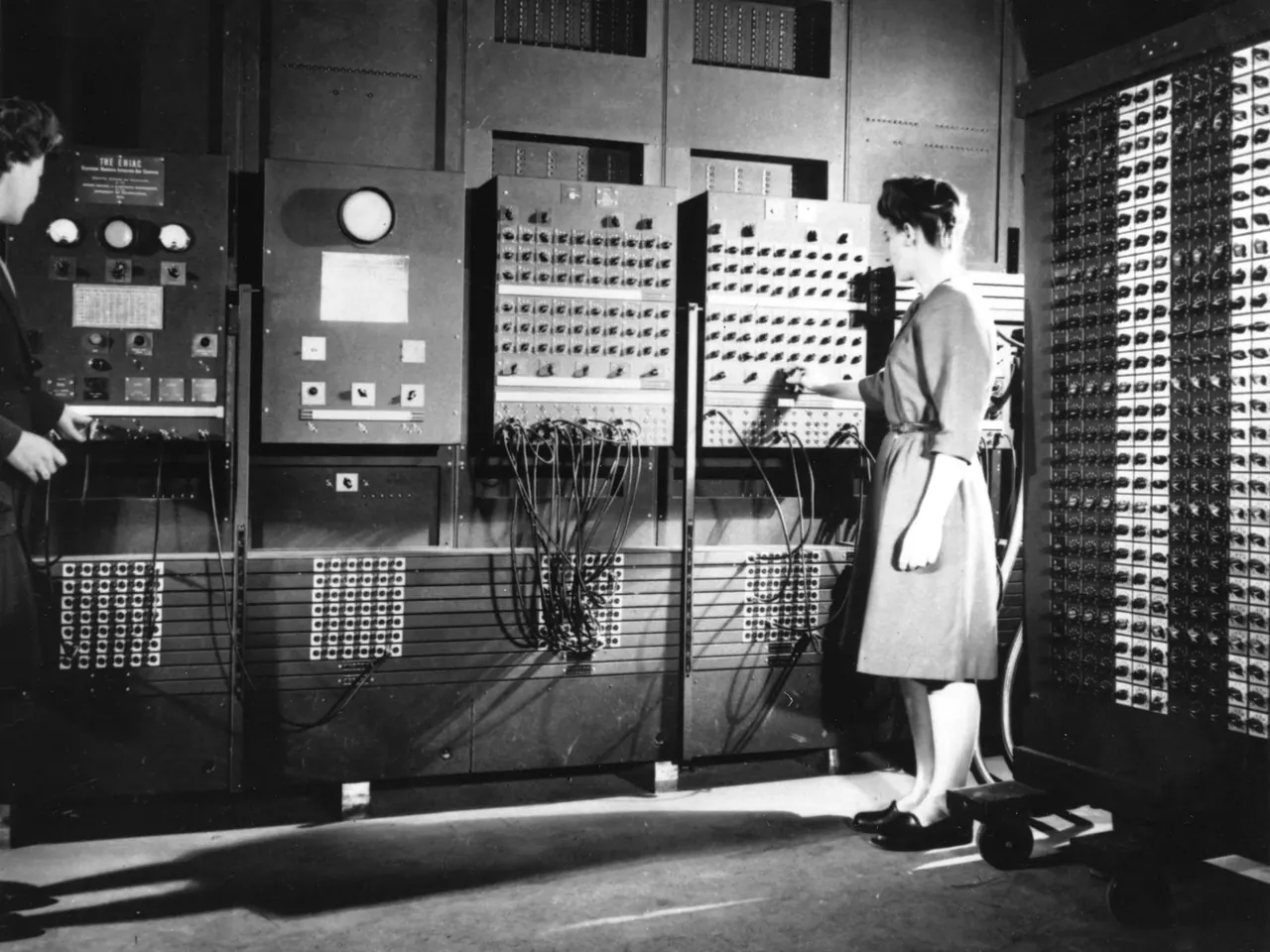 Programmers Frances Bilas and Betty Jean Jennings at ENIAC’s main control panels in 1946, a wall of cabinets covered in dials, switches and plugboard cables